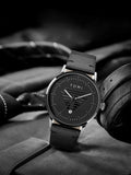 TOMI T-042 black dial men's date watch displayed with headphones and black leather strap