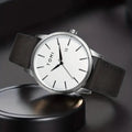 TOMI T-071 Men's Watch Date Quartz - White dial watch with silver bezel and dark grey leather strap standing on a black circular stand.